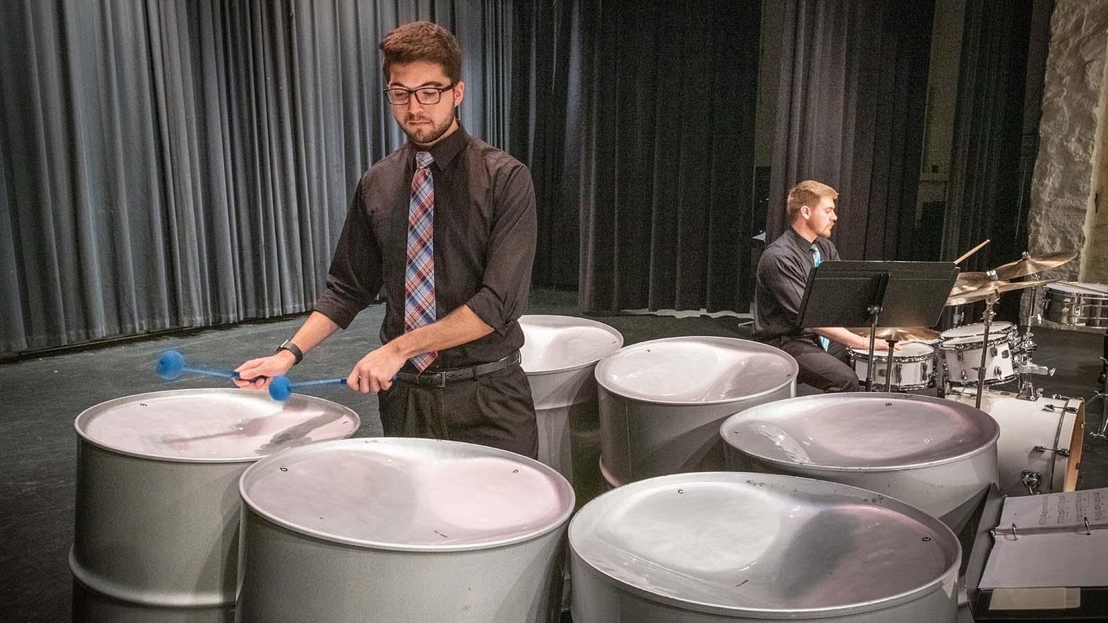 Music student playing steel pans on stage with another student behind him